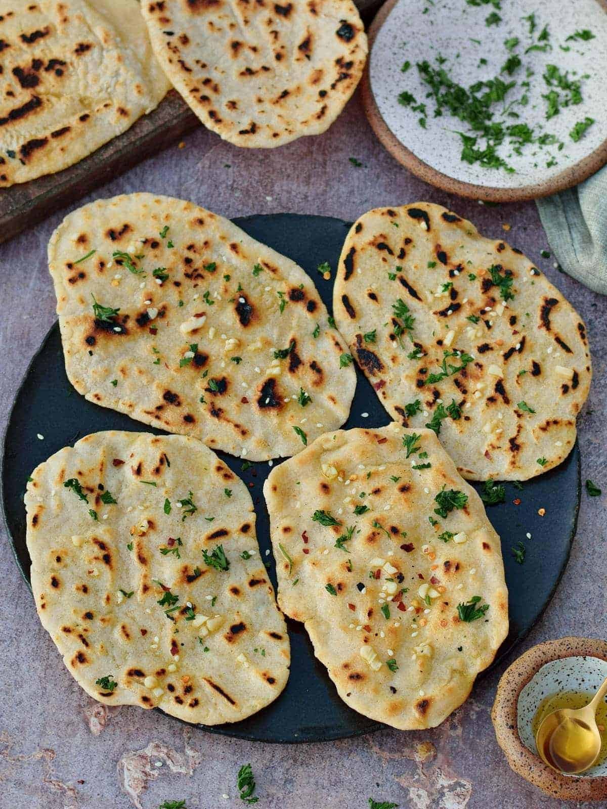 4 pieces of vegan gluten free naan on black plate with herbs and garlic